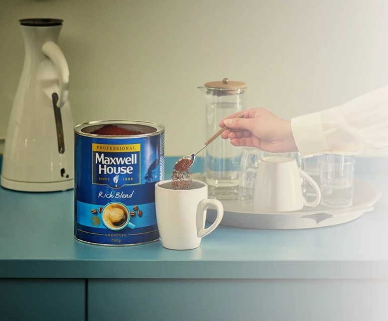 Person füllt Maxwell House Rich Blend Kaffeegranulat in eine weiße Tasse.