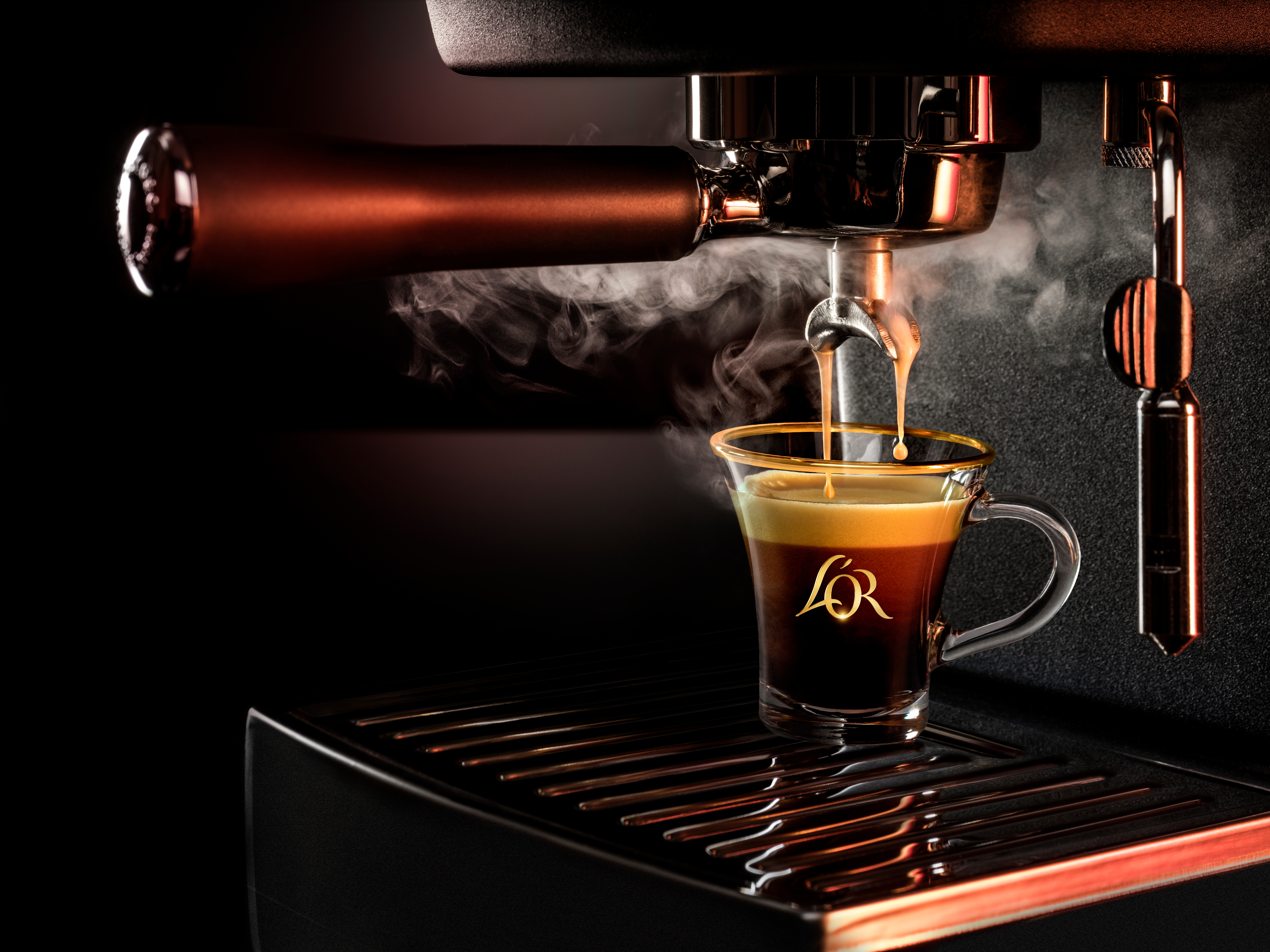 Nahaufnahme einer L'OR-Espressomaschine beim Brühen – heißer Kaffee mit Dampf in einem Glas mit Logo.